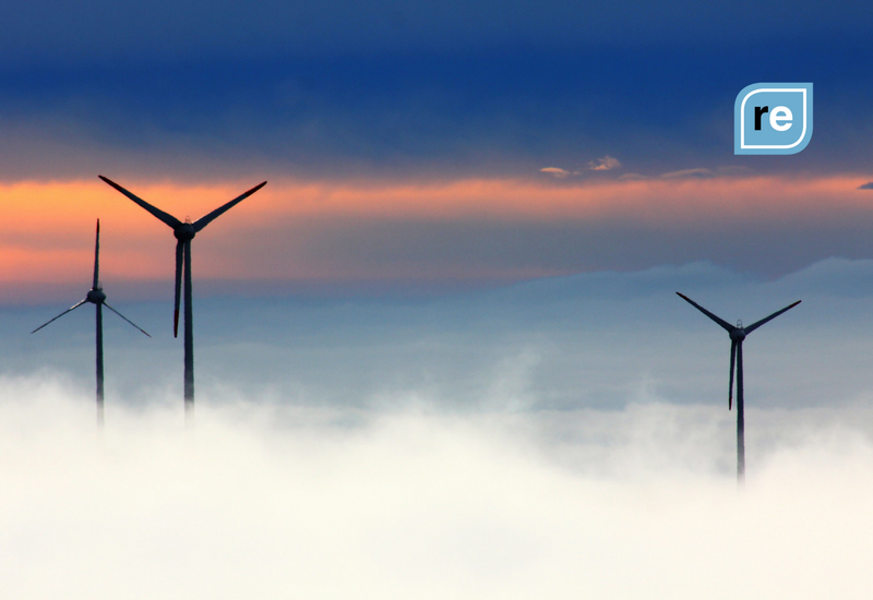 Wind turbines emerge from misty clouds at dawn, symbolizing renewable energy and sustainable productivity.