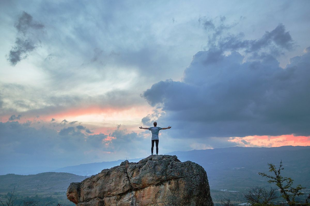 Person with arms wide open standing on a rock against a vibrant sunset, symbolizing time management success.