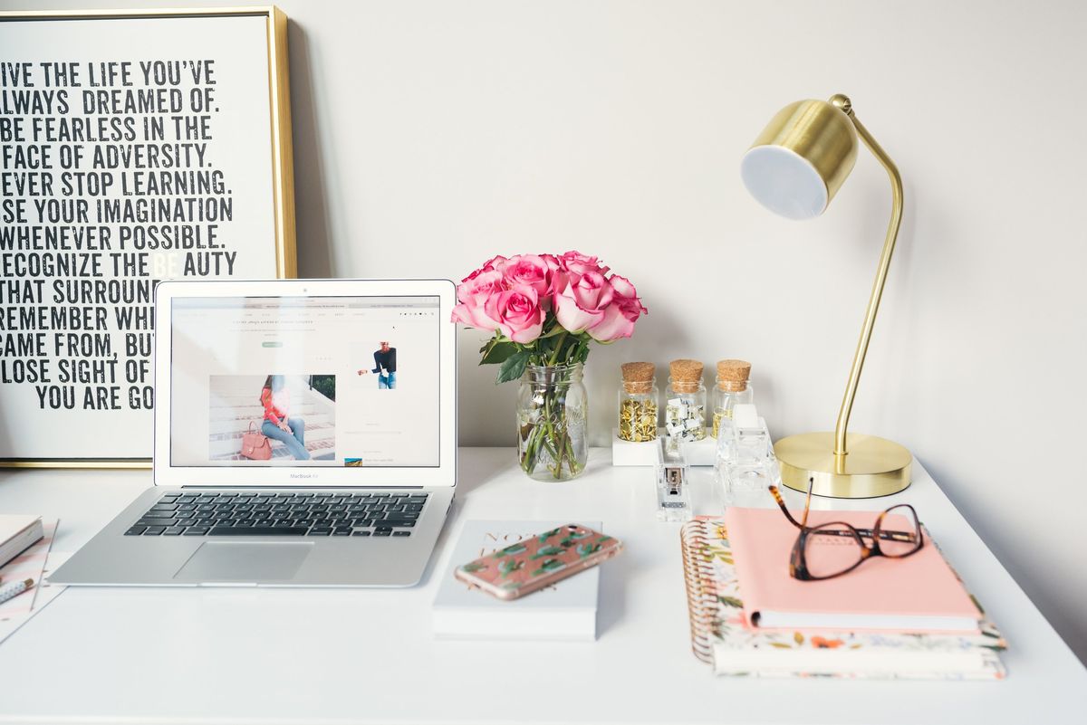 Chic workstation with an open laptop displaying a blog, fresh roses in a jar, and inspirational quote framed poster.