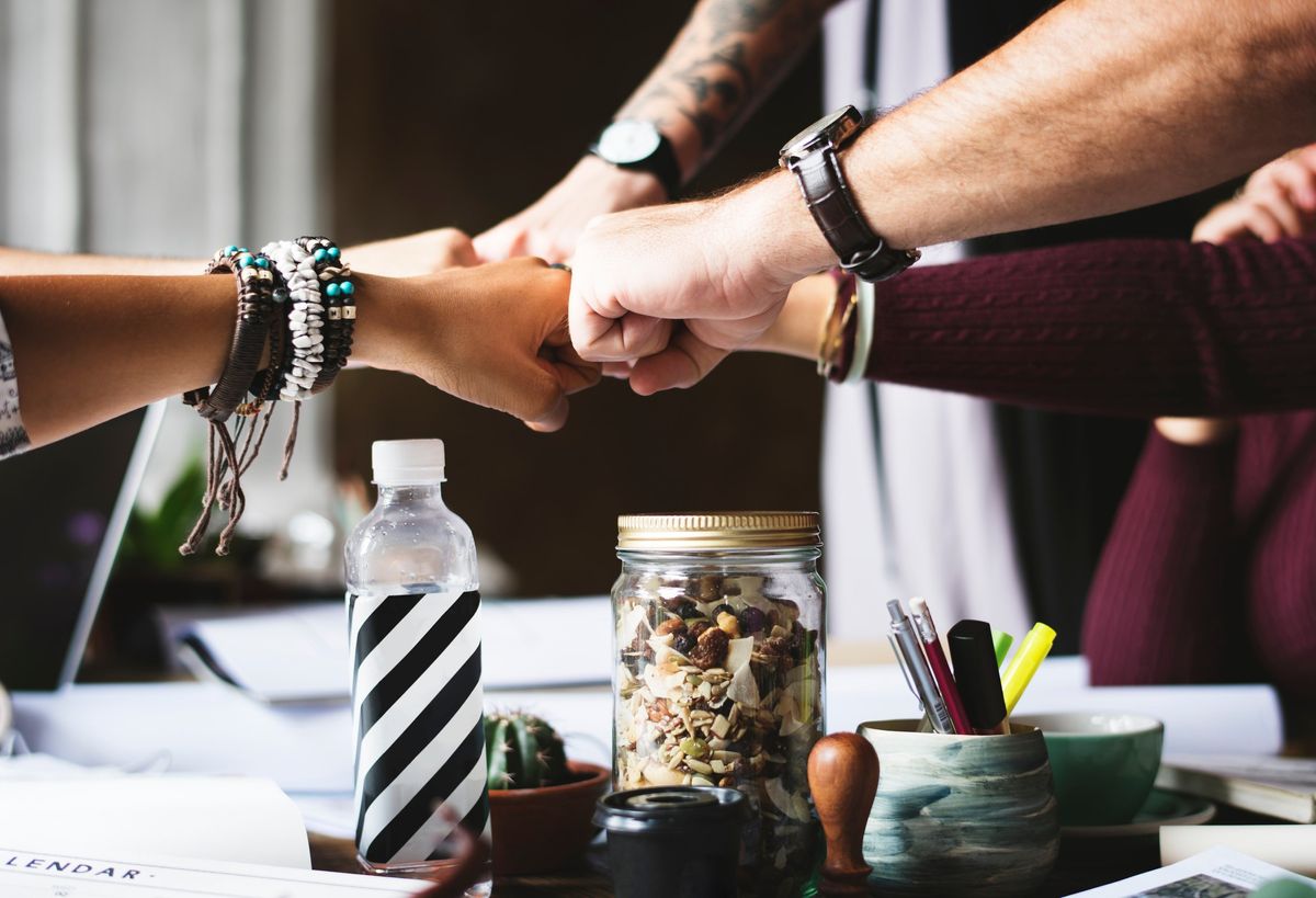 A group fist bump over a cluttered desk symbolizes teamwork and effective delegation in an AI-optimized workplace.